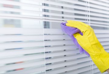 A person gently cleaning window blinds with a microfiber cloth, maintaining a spotless home environment